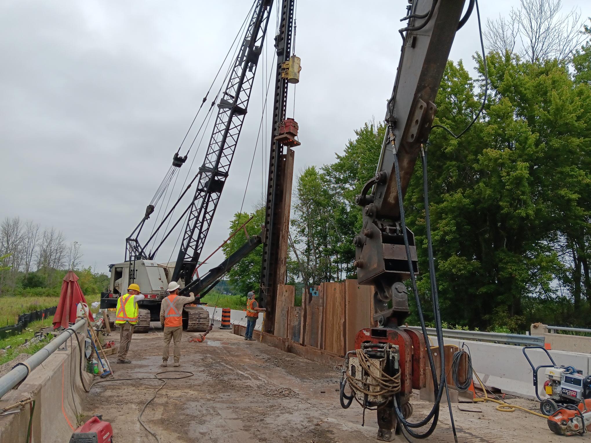 A team of three construction workers using hand gestures to direct a person operating a large piece of construction equipment.  