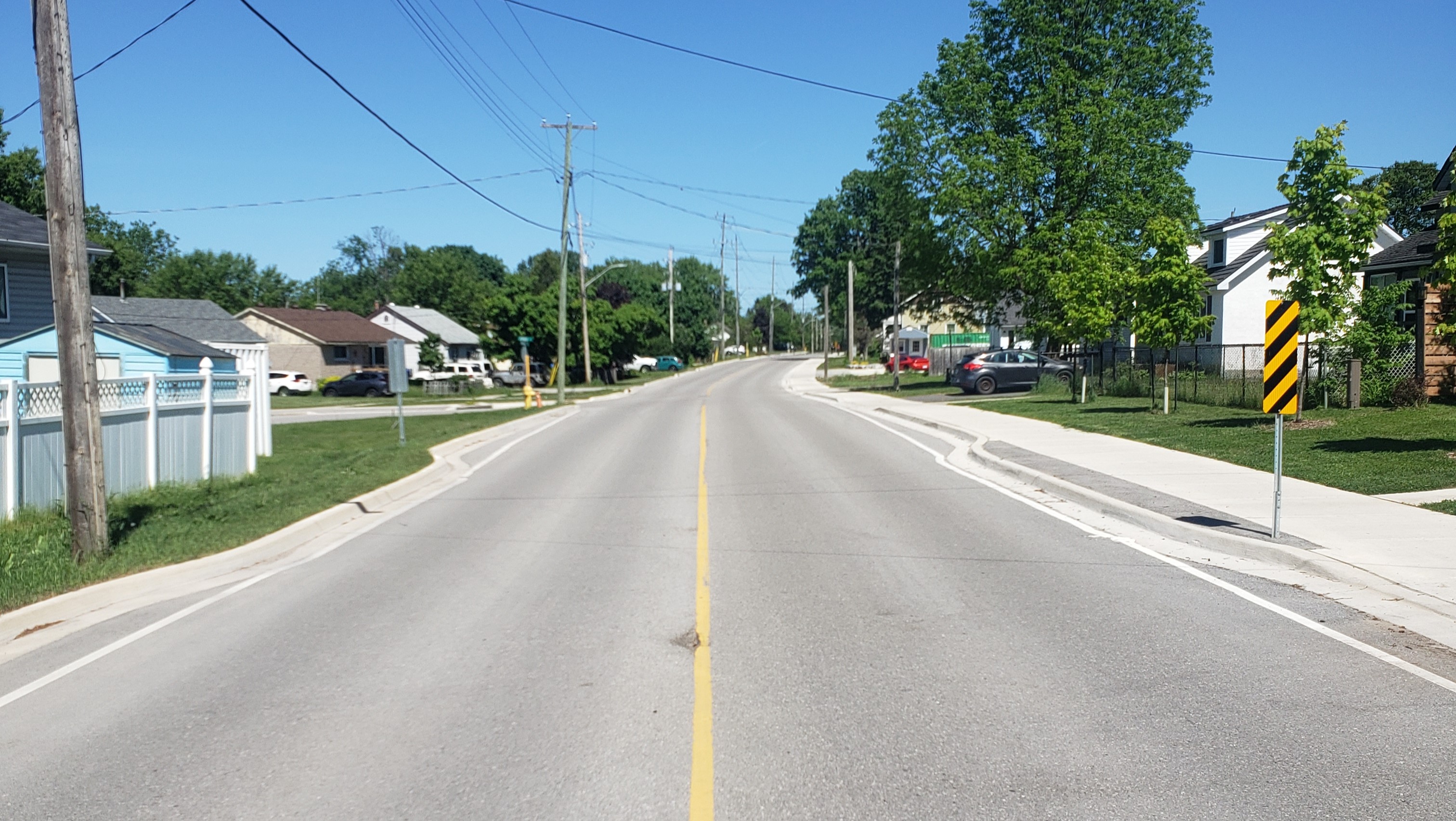 A residential street with a newly installed sidewalk and freshly paved road