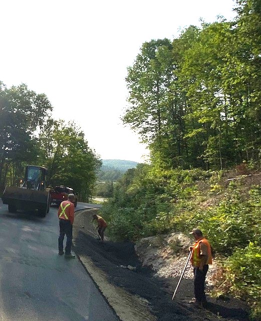 Construction workers and machinery repaving a windy rural roadway.