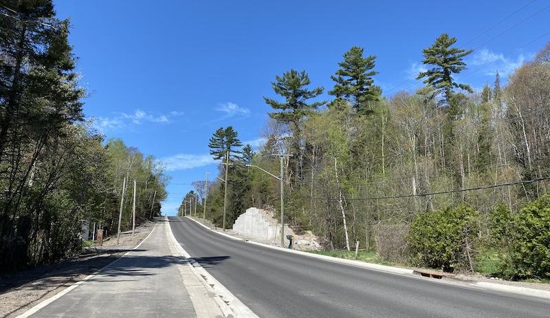 A freshly paved roadway is shown under a bright blue sky. 