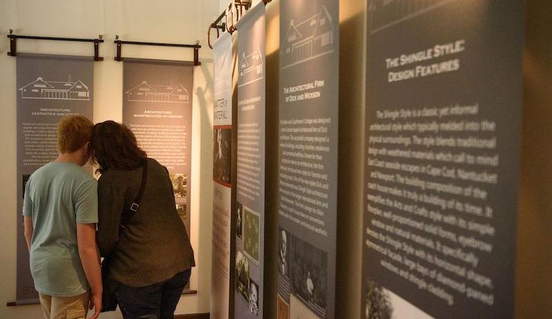 A boy and a woman stand with their backs to the camera, observing historic signage at the Coach House museum in Oakville. 