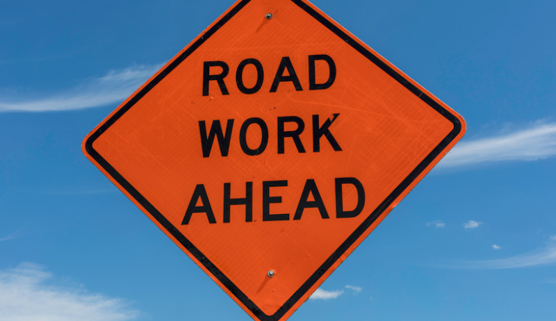 A diamond-shaped orange sign that says "road work ahead".