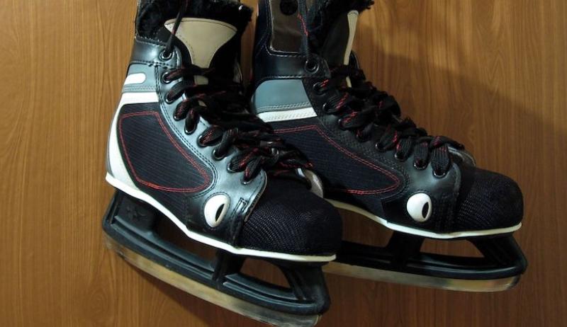 A pair of hockey skates hang on a brown wall. 