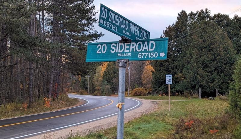 A roadway shown in a sunset with a street sign that reads "20 Sideroad River Road".