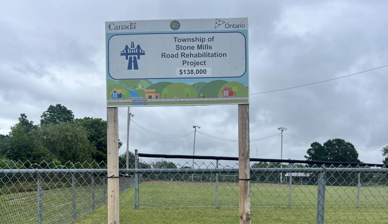 A rural roadway under an overcast sky with a project sign that says "Township of Stone Mills Road Rehabilitation Project".